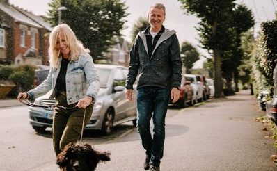 senior woman and senior man laughing while walking their dog on the streets